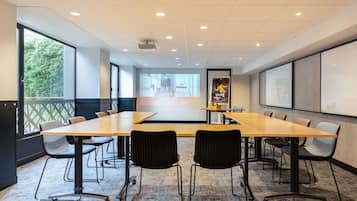 Une salle de conférence avec une longue table, des chaises, un écran de projection et une grande fenêtre.