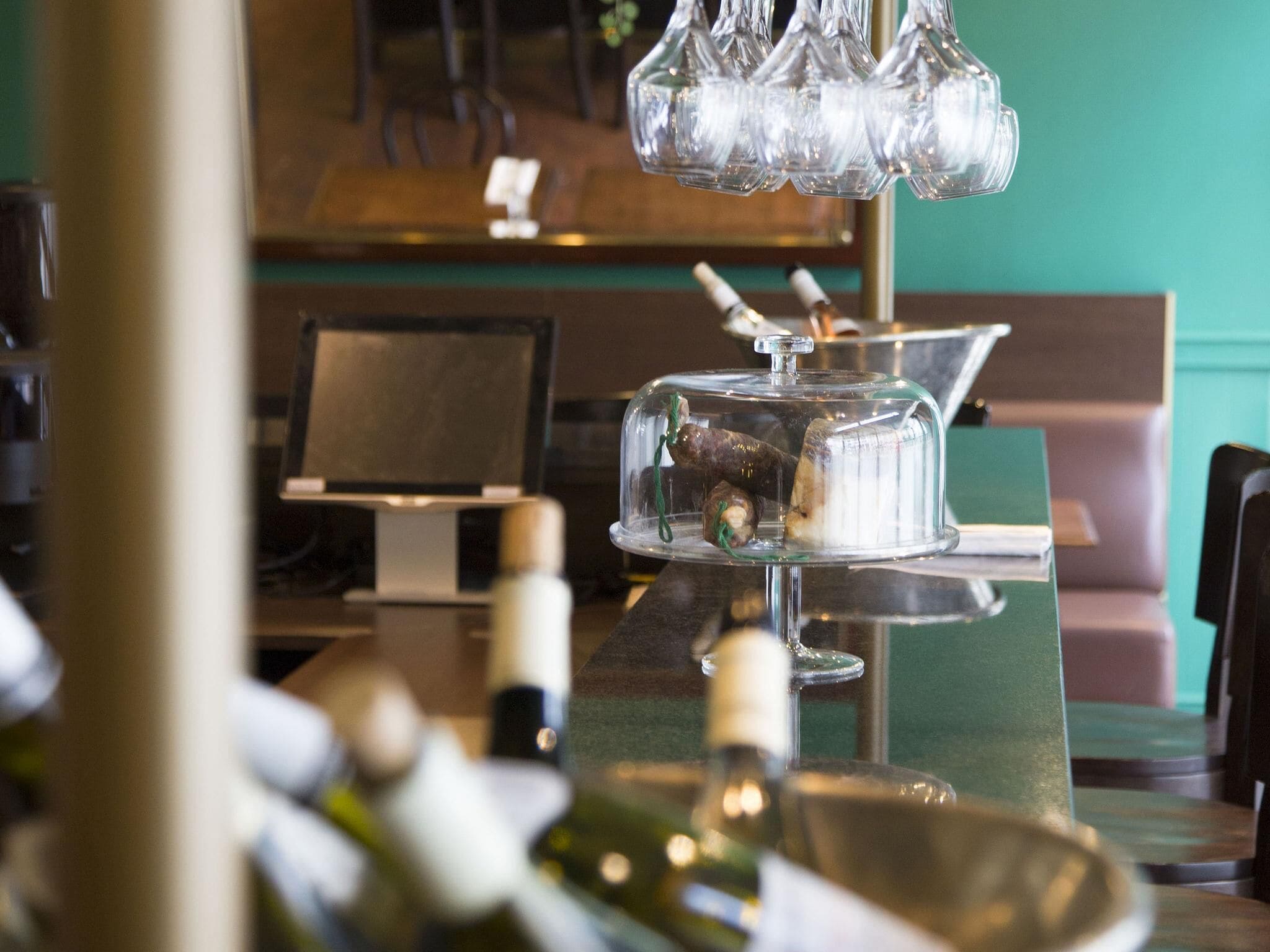 Zona de bar con una vitrina que contiene botellas, una botella de vino sobre la barra y una pared verde al fondo.