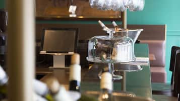Un espace bar avec un présentoir en verre contenant des bouteilles, une bouteille de vin posée sur le comptoir et un mur vert en arrière-plan.