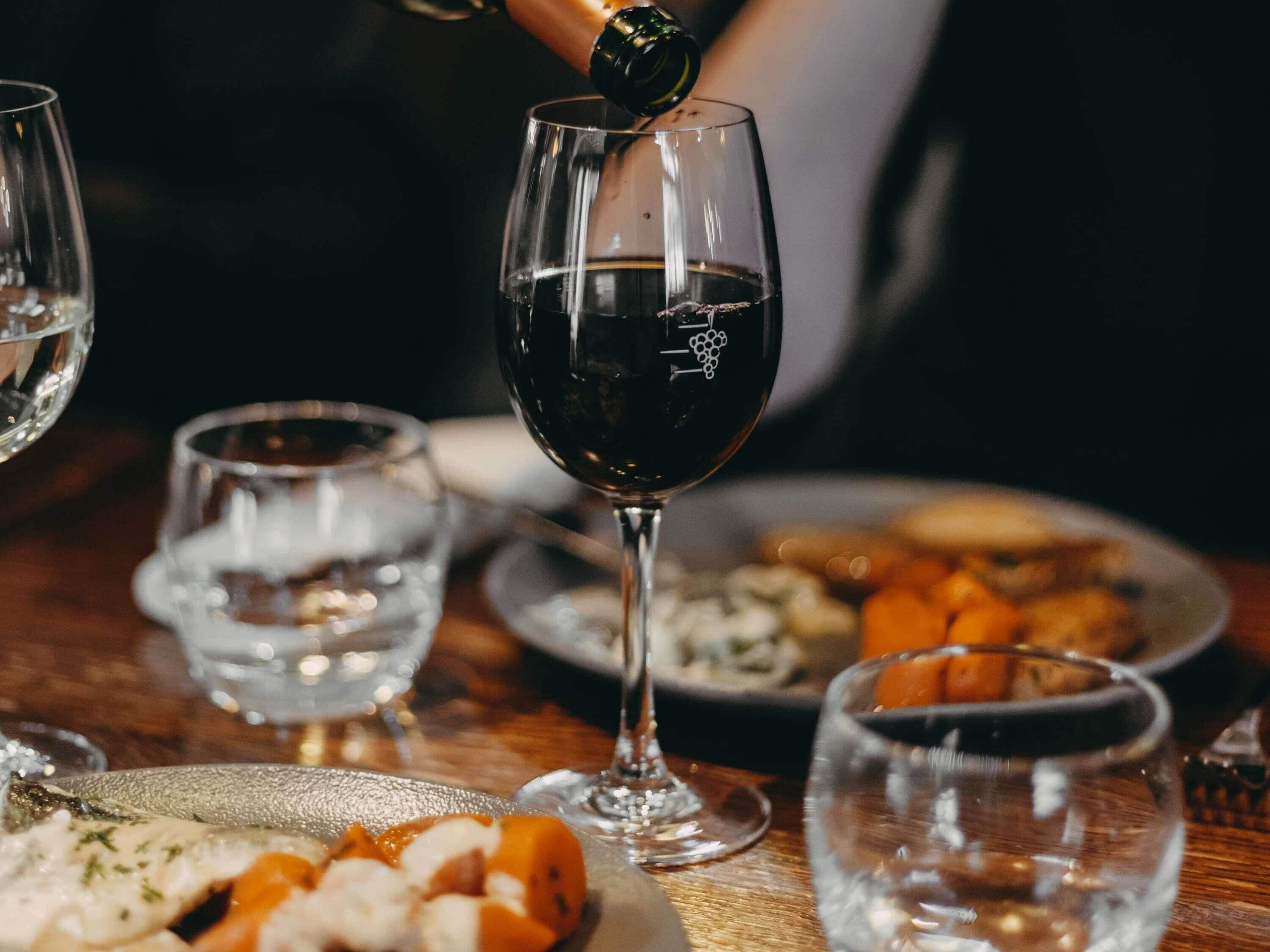 Une table à manger avec un verre de vin rouge, une assiette de nourriture et un verre d’eau.