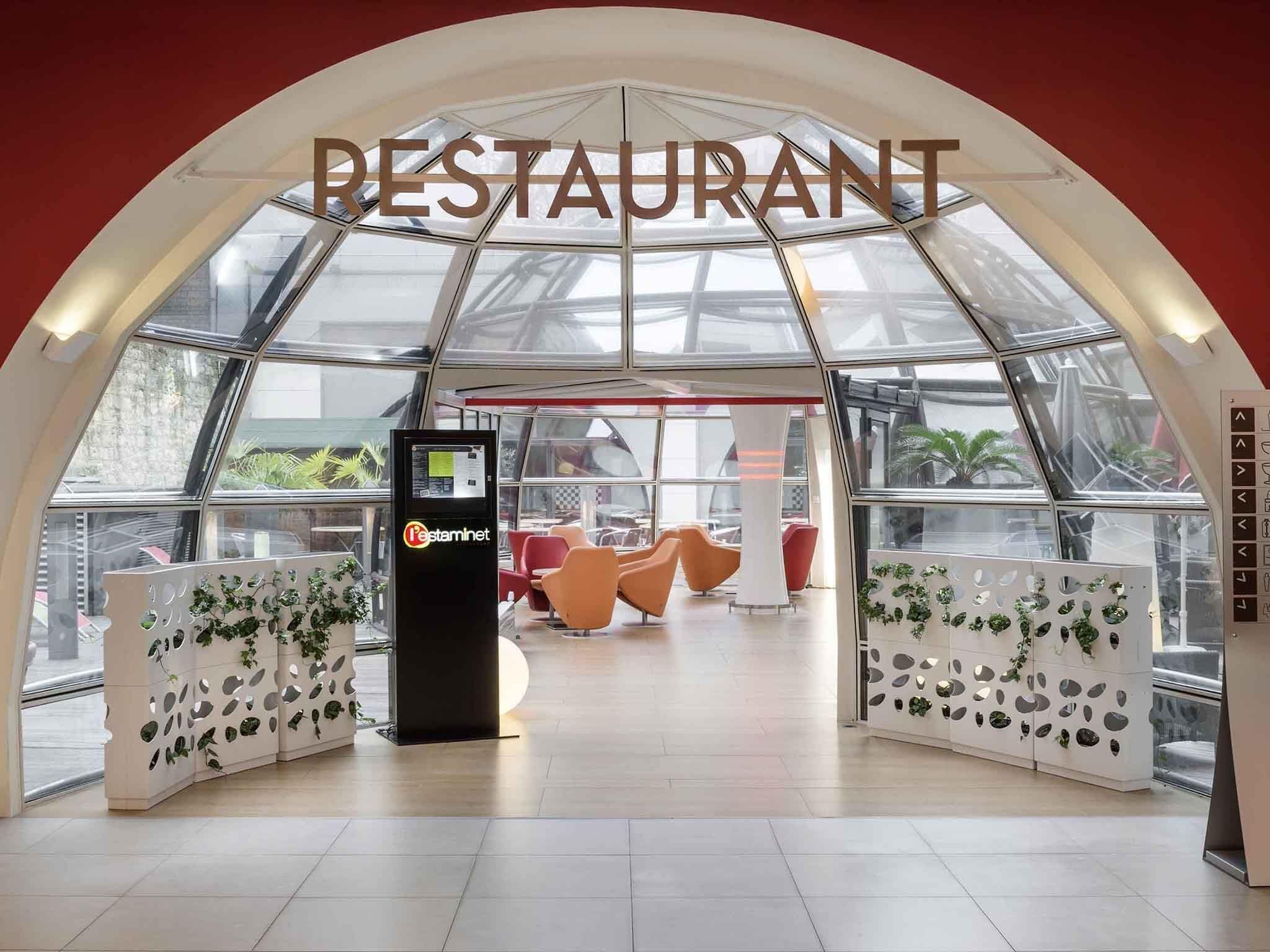 A restaurant with a modern, arched glass ceiling and a self-service kiosk.