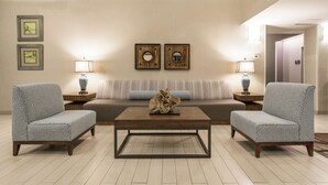 A modern living room with a sofa, two armchairs, a coffee table, and two wall-mounted lamps. There are two framed pictures on the wall. - Hampton Inn Morehead City (Morehead City)