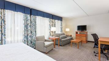 A hotel room with a bed, a sofa, a desk, a chair, a television, and a telephone.