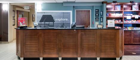 A reception desk with a wooden finish, a large 'explore.' sign, and a display of various products on shelves to the right.