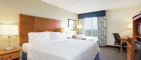 Habitación de hotel con una cama grande, un escritorio, una silla, un televisor y una ventana con cortinas.