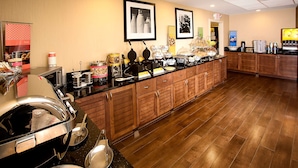 A buffet setup with various food items, a coffee station, and a refrigerator. - Hampton Inn Morehead City (Morehead City)