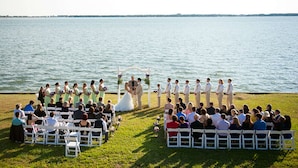 A wedding ceremony by a lake with guests seated on white chairs facing the couple. - Hampton Inn Morehead City (Morehead City)