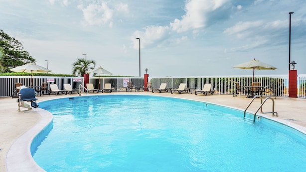 A swimming pool with lounge chairs and umbrellas, surrounded by a fence and palm trees. - Hampton Inn Morehead City (Morehead City)