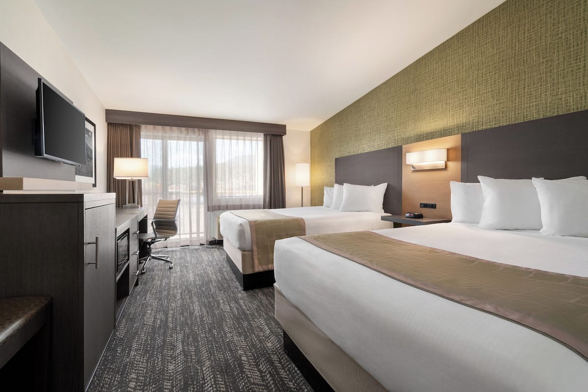 A hotel room with two beds, a desk, a TV, and a large window with curtains.
