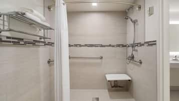 Ein modernes Badezimmer mit Dusche, Ablagefläche, Handtuchhalter und Haltegriff.