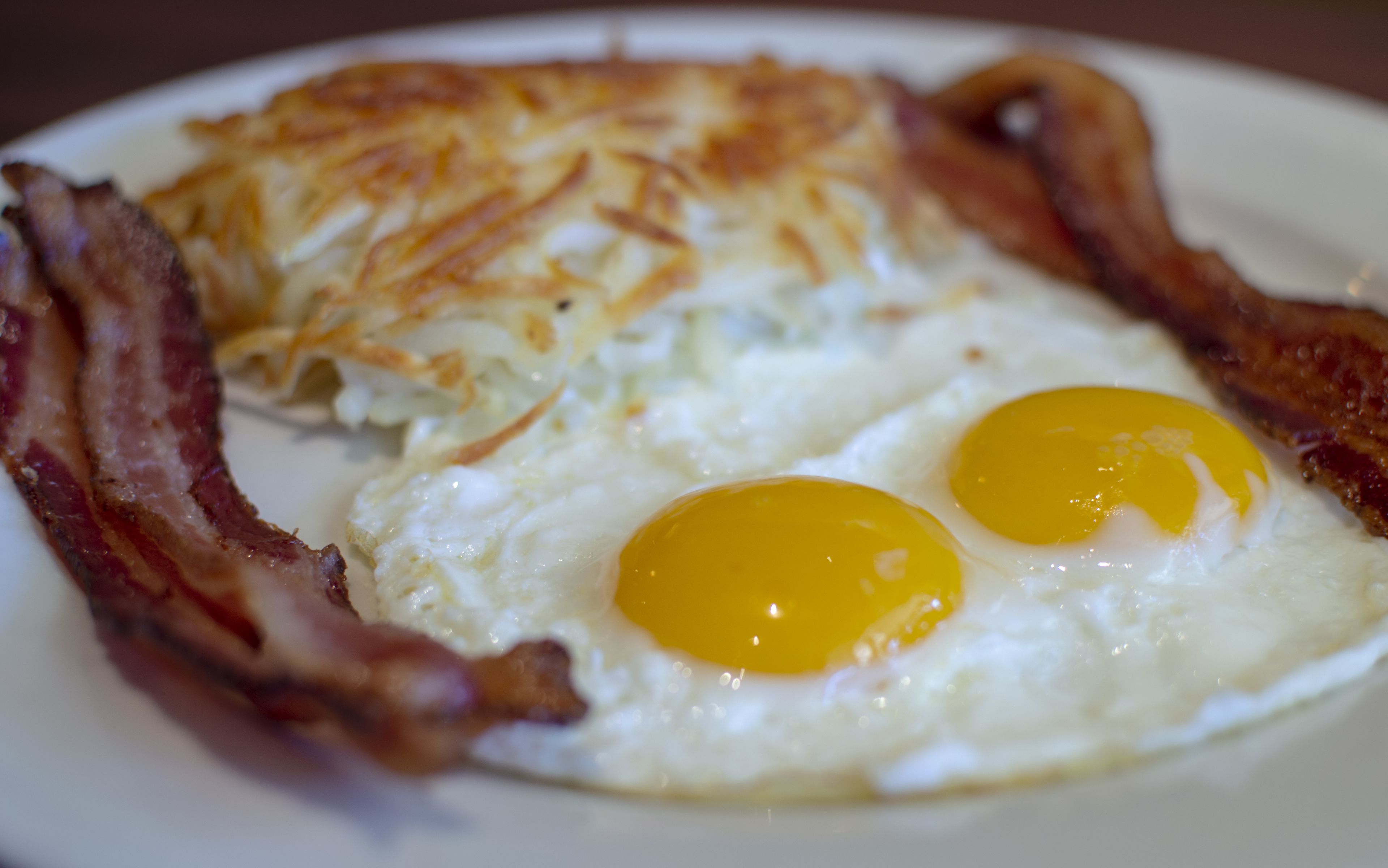 Een ontbijtbord met twee gebakken eieren en hashbrowns, omringd door baconreepjes.