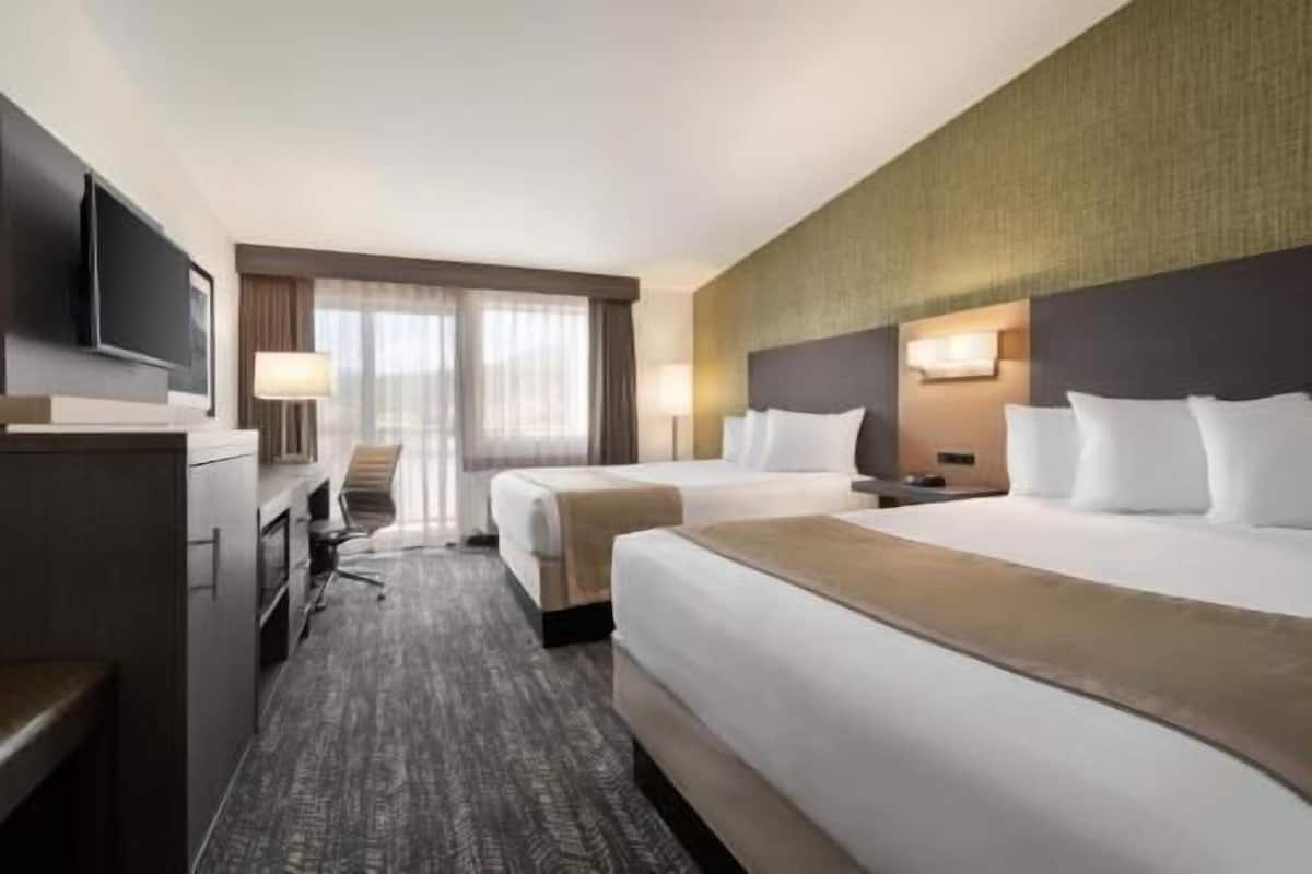 A hotel room with two beds, a desk, a TV, and a view of the outdoors.