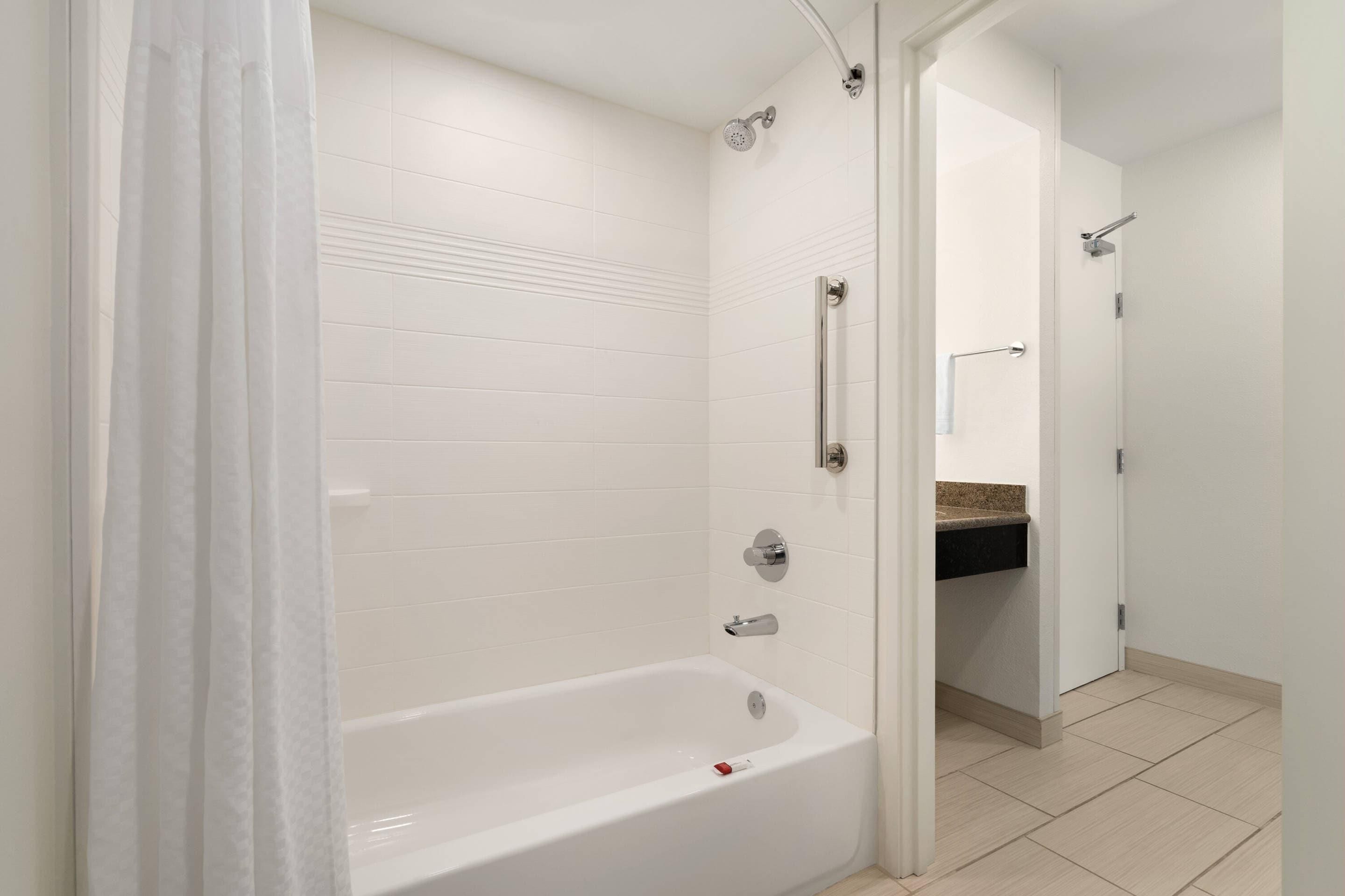 A modern bathroom with a white bathtub, a shower, and a vanity with a countertop.