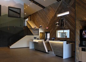 A modern reception area with a wooden wall, a reception desk, a staircase, and a television screen.