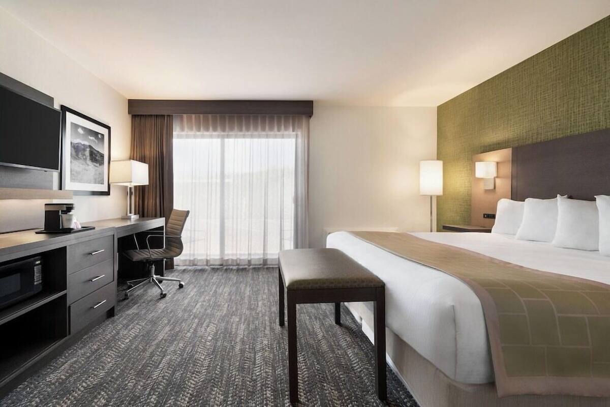A hotel room with a bed, a desk with a chair, a television, and a window with curtains.