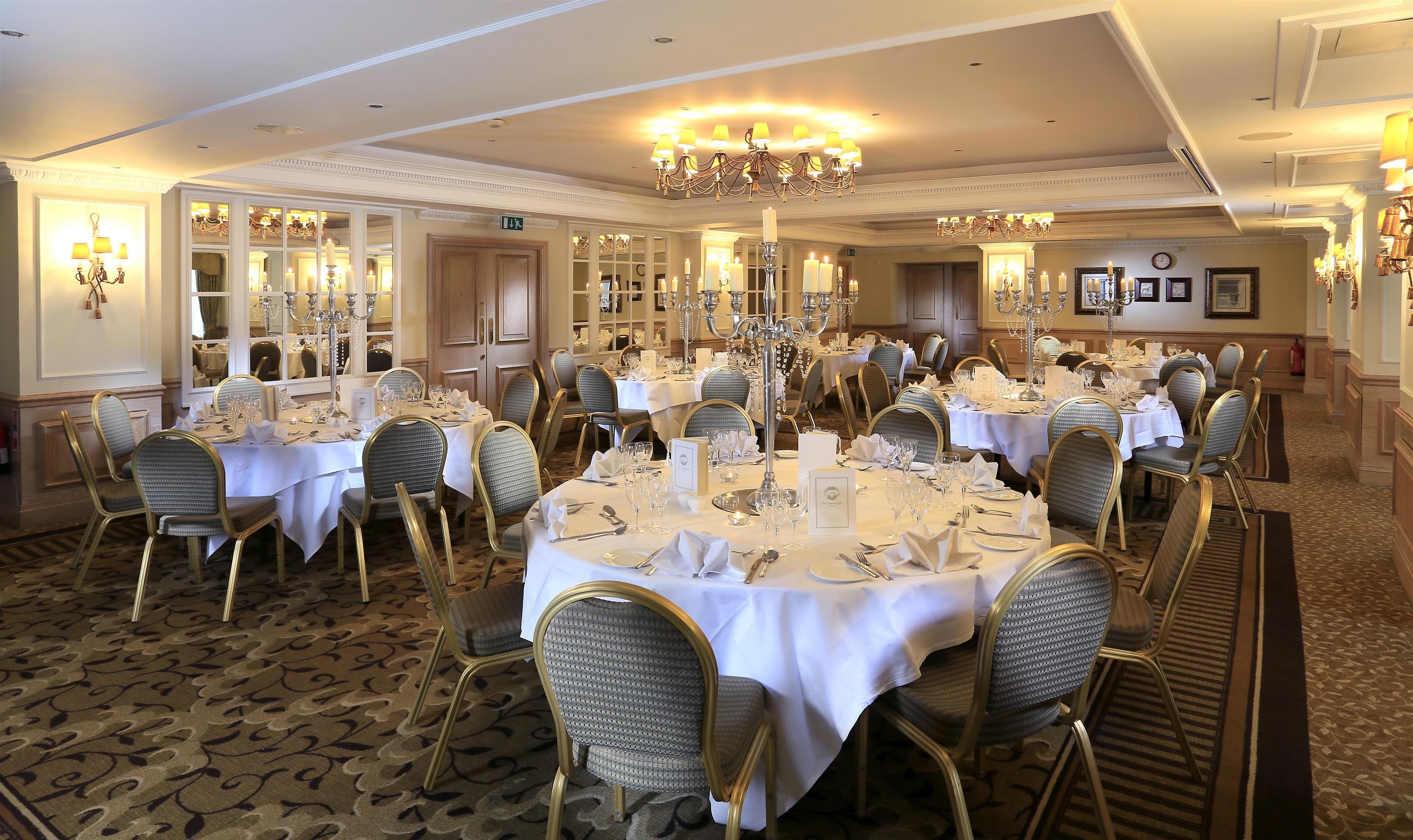 A formal dining room with round tables, gold chairs, and chandeliers.