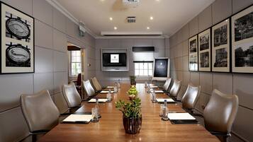 Una sala de conferencias con una mesa larga, sillas de cuero, cuadros enmarcados y una pantalla de televisión.