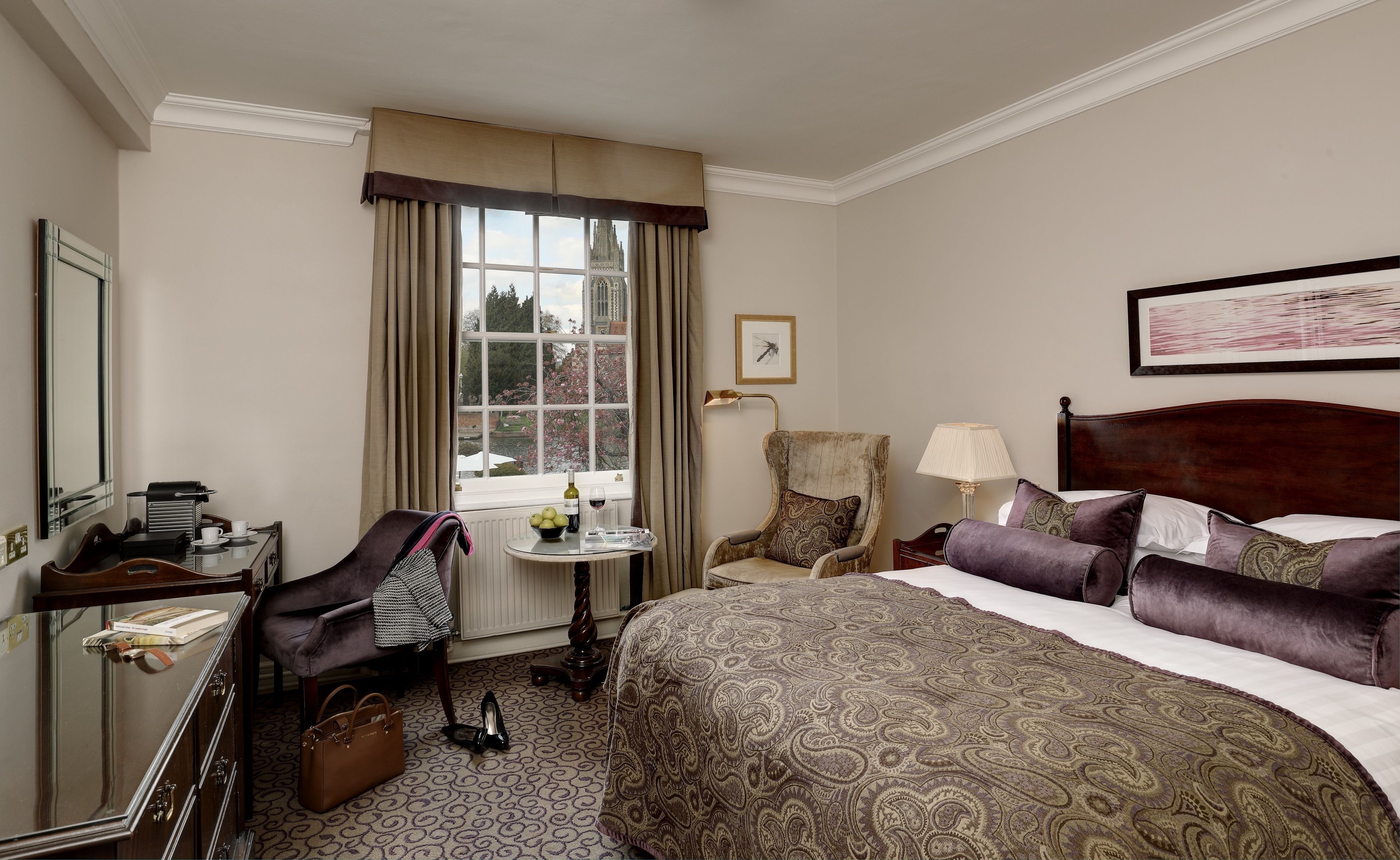 Hotelkamer met een bed, een stoel, een tafel met een lamp, een raam met gordijnen en uitzicht op een gebouw.