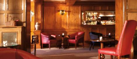 A cozy bar area with wooden paneling, red leather chairs, and a bar counter with bottles.