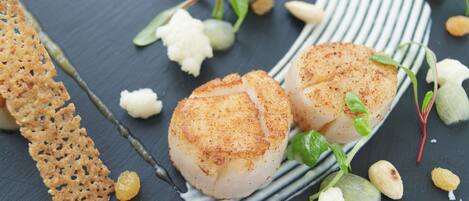 A plate with seared scallops, garnished with microgreens and a slice of lemon.