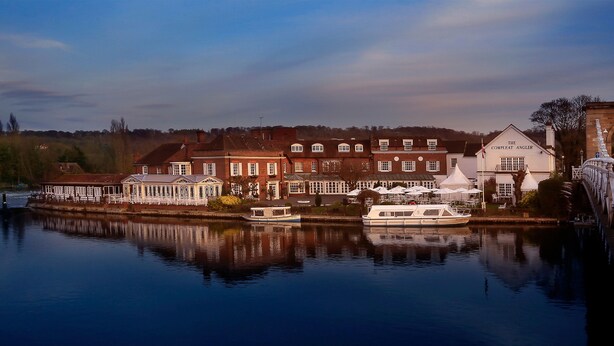 A riverside building with a covered patio area and a boat docked nearby. - Macdonald Compleat Angler (Marlow)