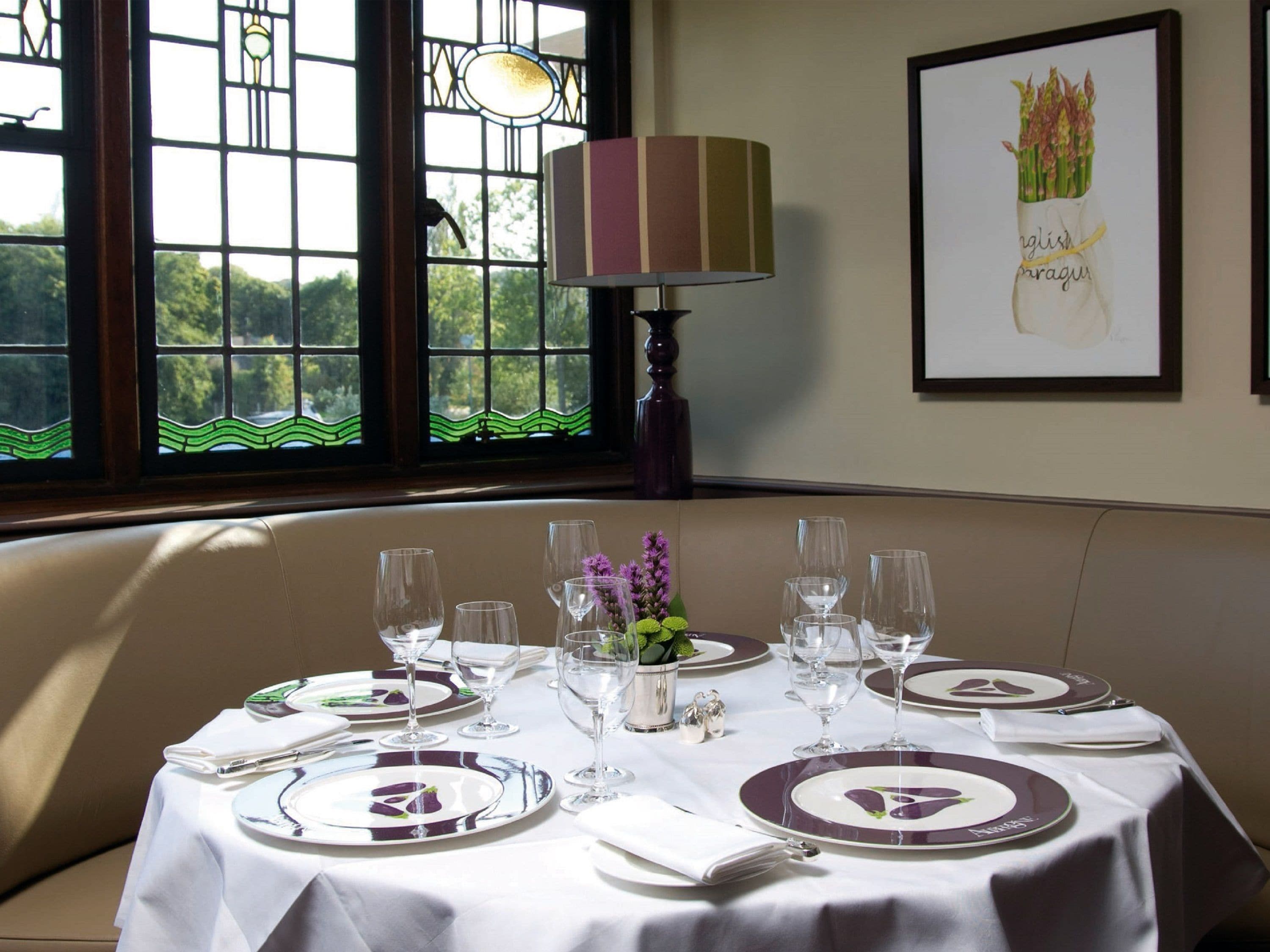 A dining table set with plates, glasses, and cutlery, a vase with flowers, and a lamp.