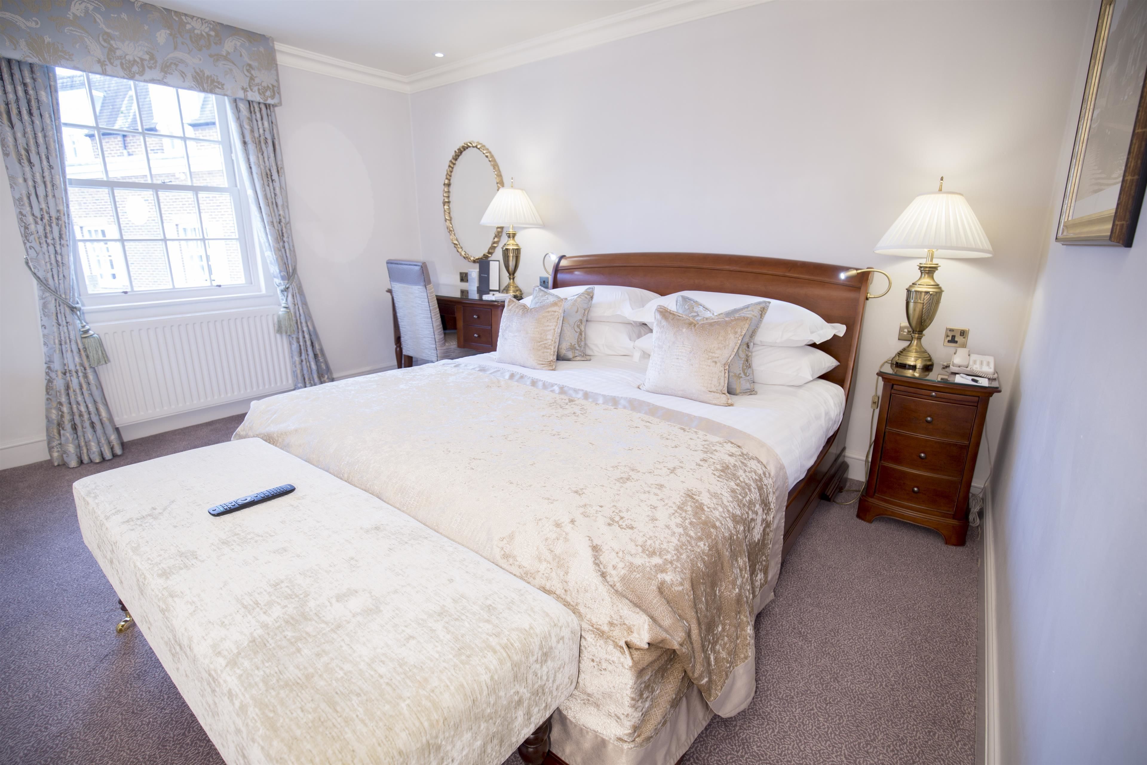 A neatly arranged bedroom with a large bed, bedside lamps, a mirror, and a window with curtains.