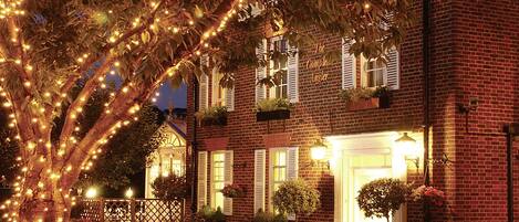 A brick building with a welcoming entrance, outdoor seating, and string lights.