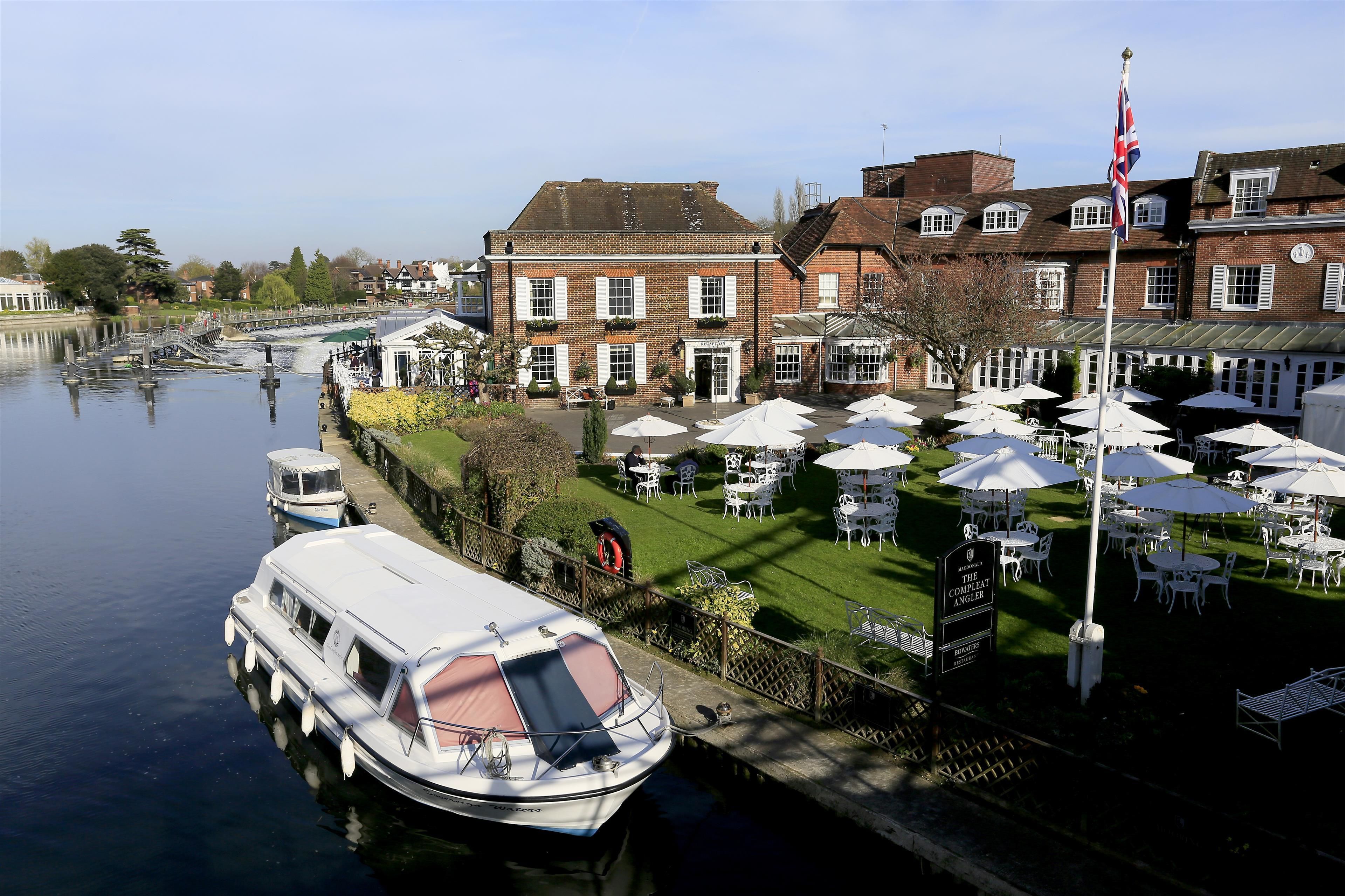 A riverside hotel with outdoor seating, a flag, and a boat docked nearby.