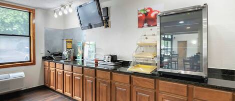A kitchenette with a microwave, toaster, waffle maker, and a refrigerator.