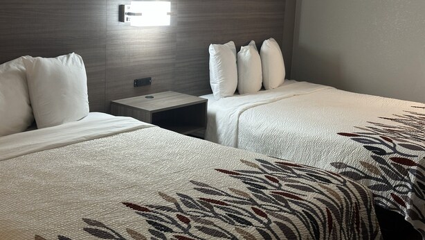 A hotel room with two beds, a nightstand, and a wall-mounted light. - Red Roof Inn & Suites Middleborough (Middleborough)