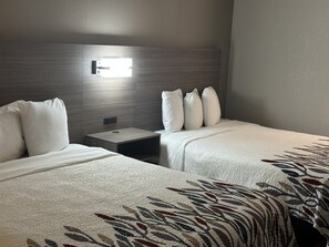 Une chambre d’hôtel avec deux lits, une table de chevet et une lampe fixée au mur.