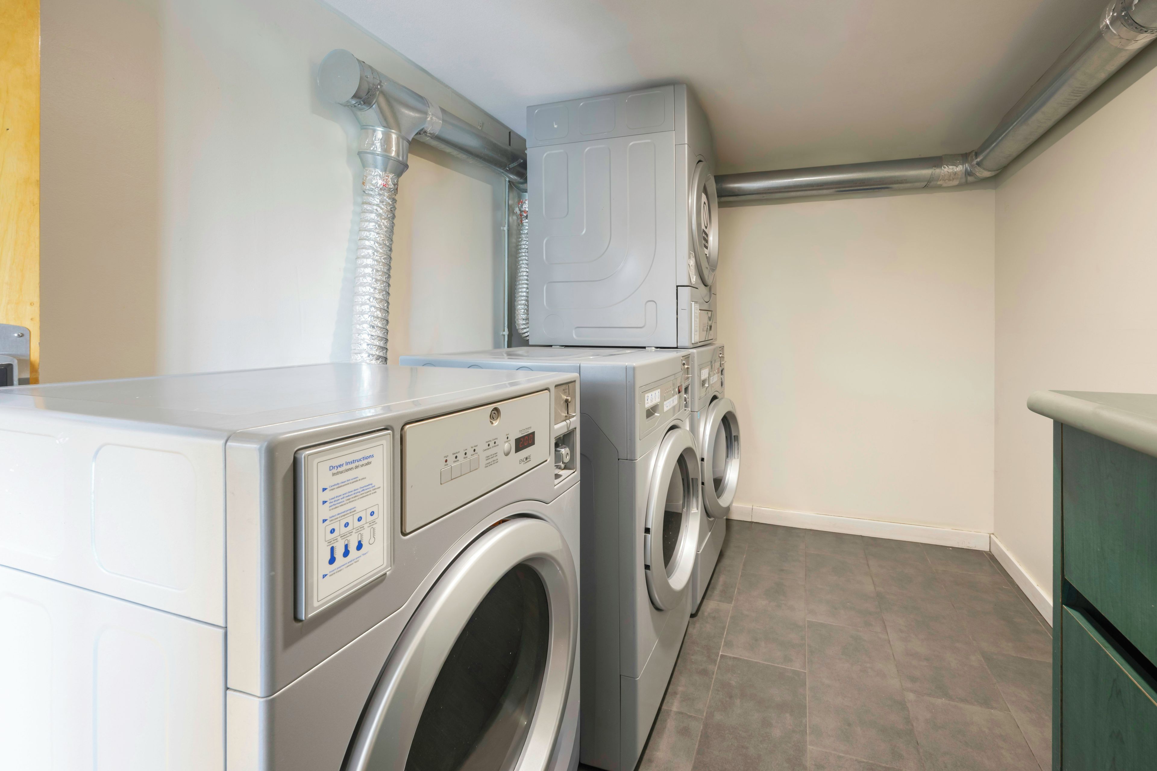 A laundry room with a front-loading washer and dryer, a vent system above, and a green cabinet to the right.