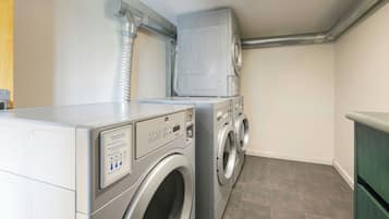 A laundry room with a front-loading washer and dryer, a vent system above, and a green cabinet to the right.