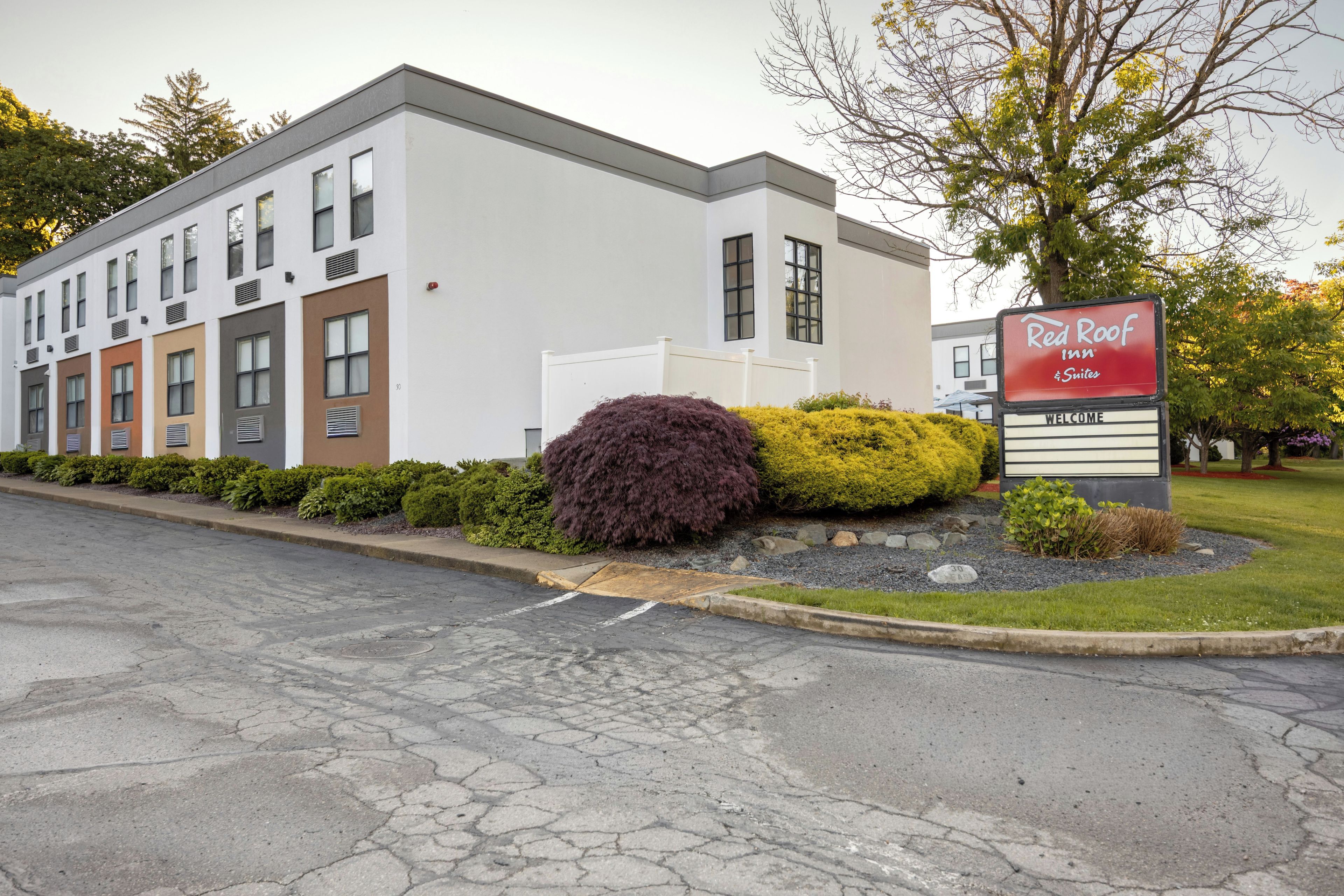 Ein Red Roof Inn mit moderner Fassade, einem angelegten Vorgarten und blauem Himmel.