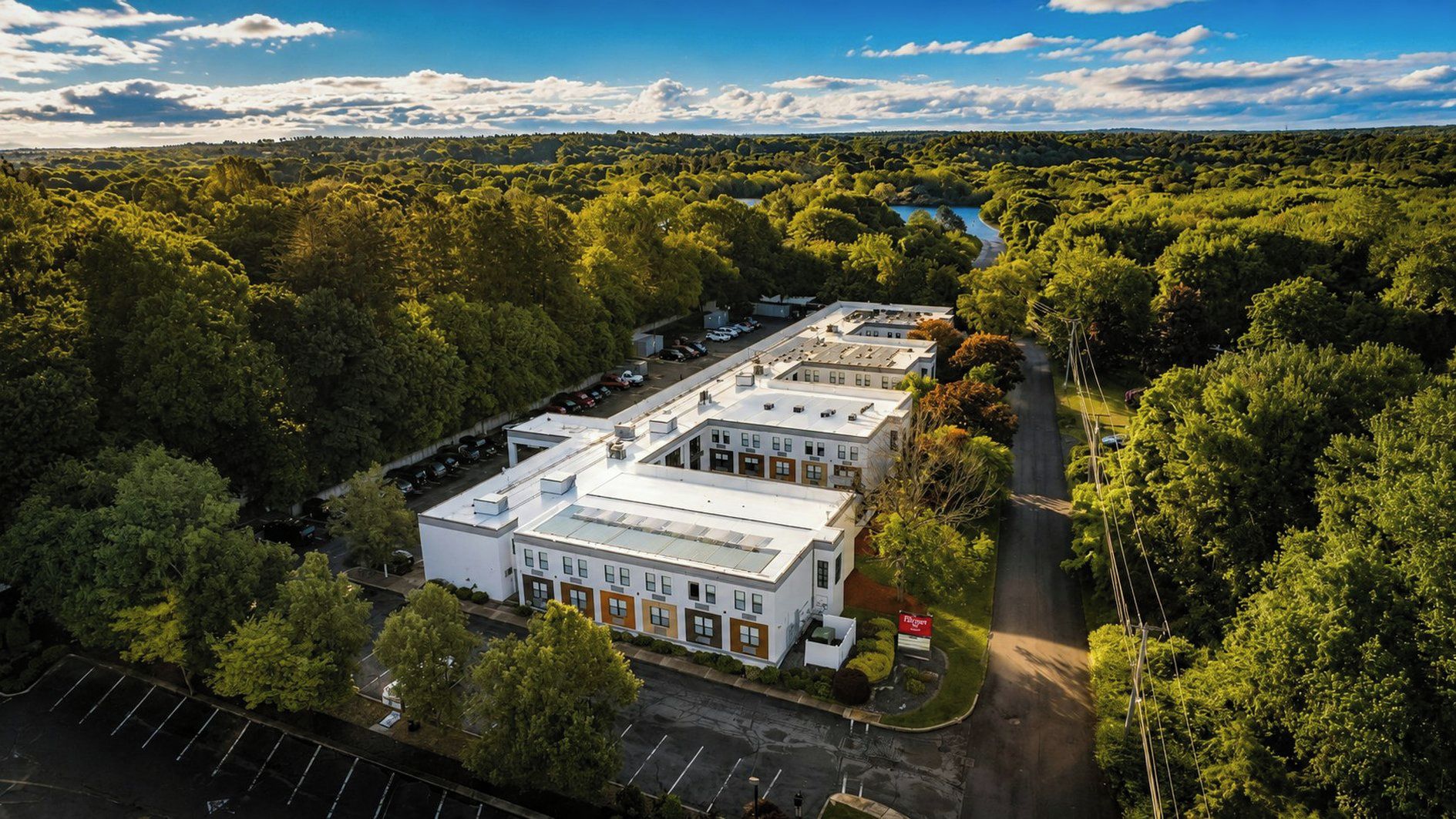 A building with a flat roof, surrounded by dense greenery and a body of water in the background.