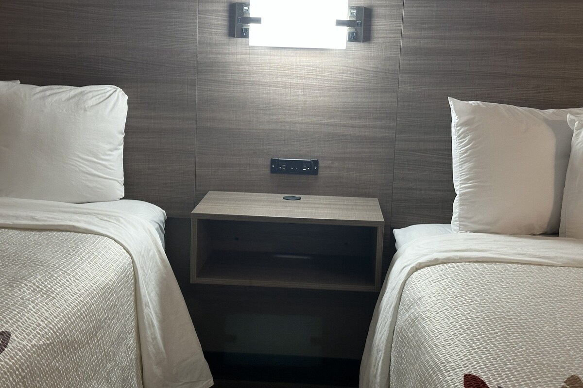 A hotel room with two beds, a nightstand, and a wall-mounted light fixture.