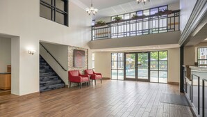 Un interior espacioso con una escalera, un balcón con plantas y vistas al exterior.