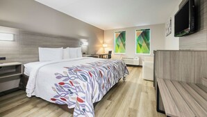 Habitación de hotel con cama, mesita de noche, escritorio, silla y televisor montado en la pared.