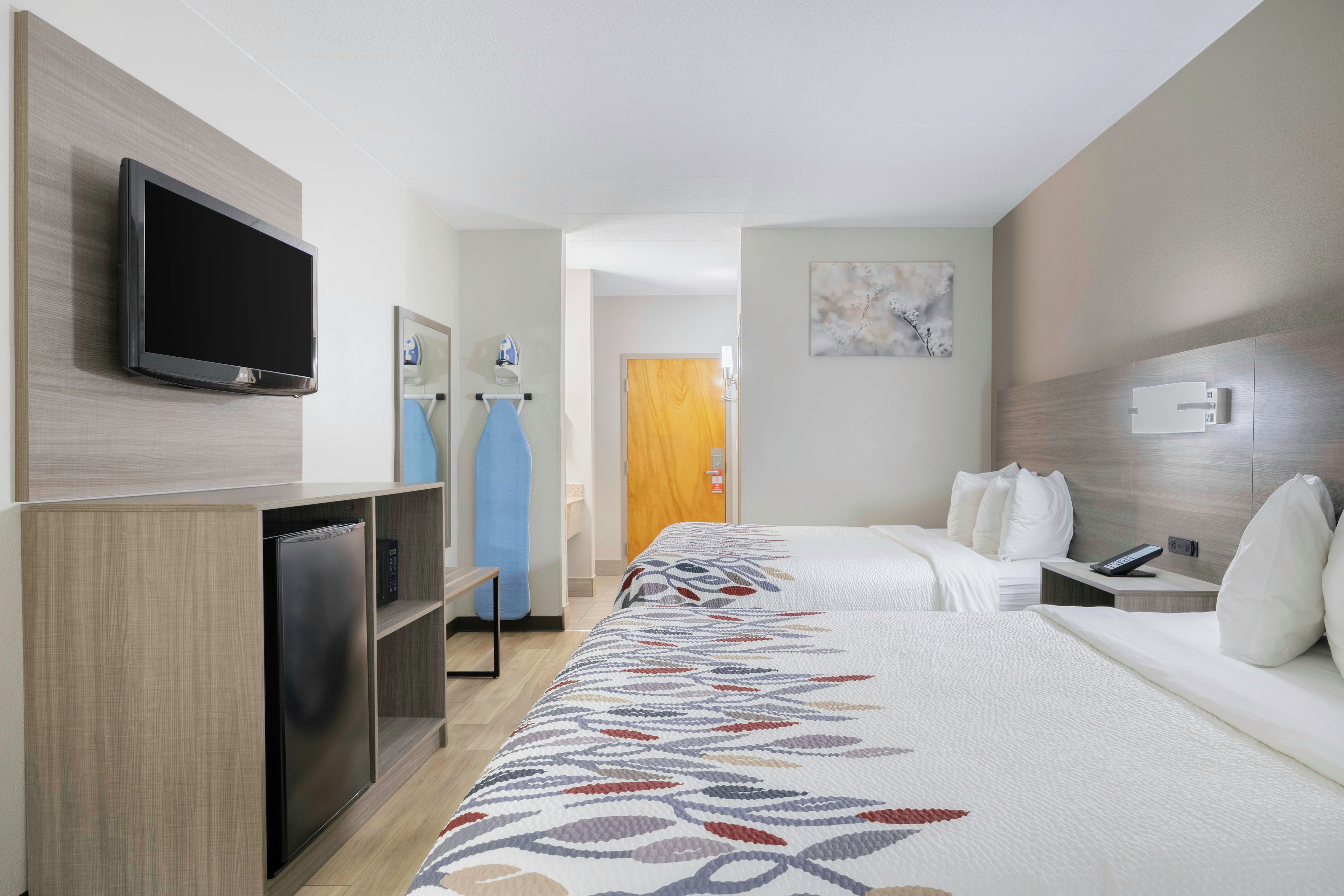 A hotel room with a bed, a television, a minibar, a desk with a phone, and a door leading to another room.