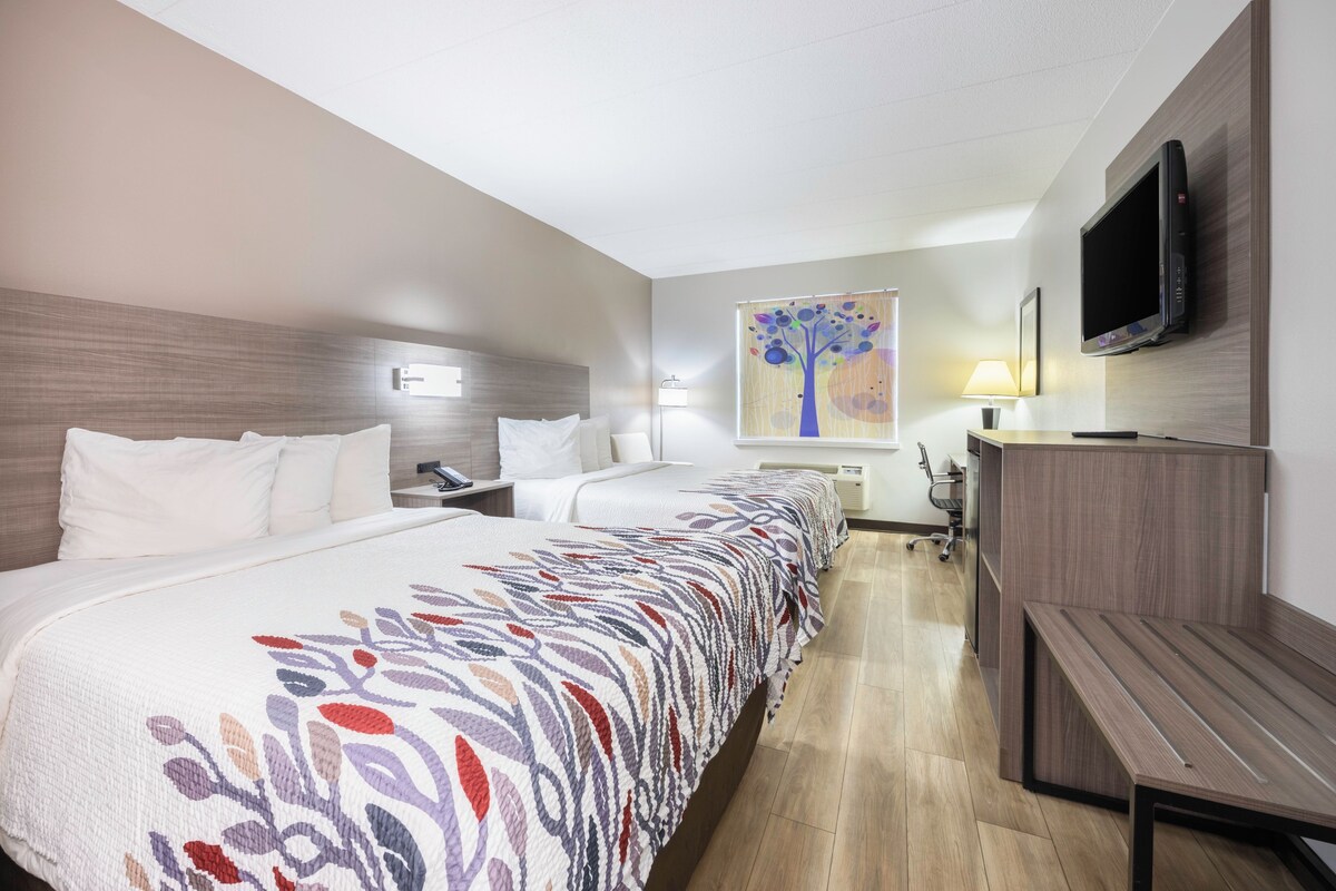 Une chambre d’hôtel avec deux lits, un bureau, une télévision et un tableau au mur.