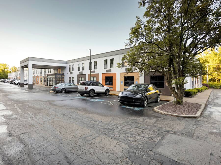Un parking avec plusieurs voitures, un bâtiment au design moderne et un arbre sur la droite.