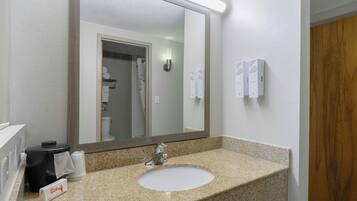 A bathroom with a granite countertop sink, a mirror, a towel dispenser, and a hand soap dispenser.