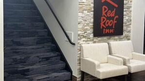 A staircase with a handrail, a wall with a stone pattern, and a chair. - Red Roof Inn & Suites Middleborough (Middleborough)