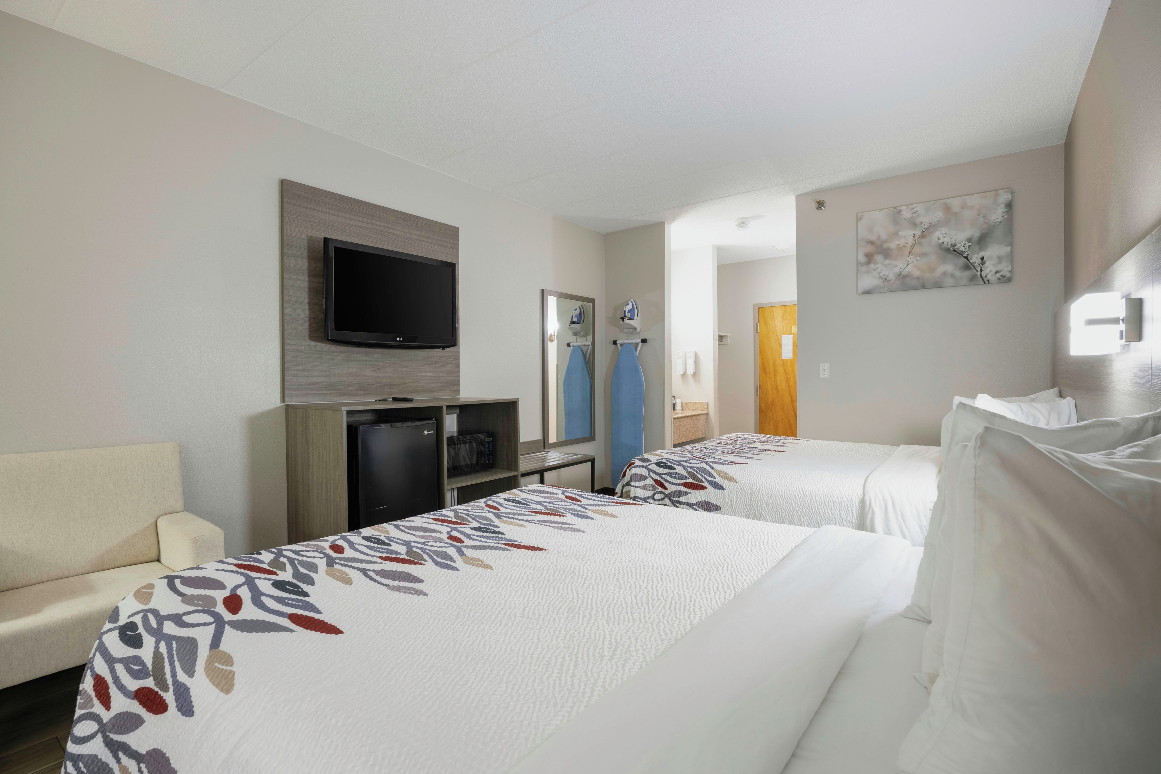 A hotel room with two beds, a TV, a desk with a computer, and a bathroom visible through an open door.