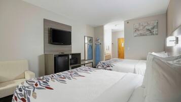 A hotel room with two beds, a TV, a desk with a computer, and a bathroom visible through an open door.