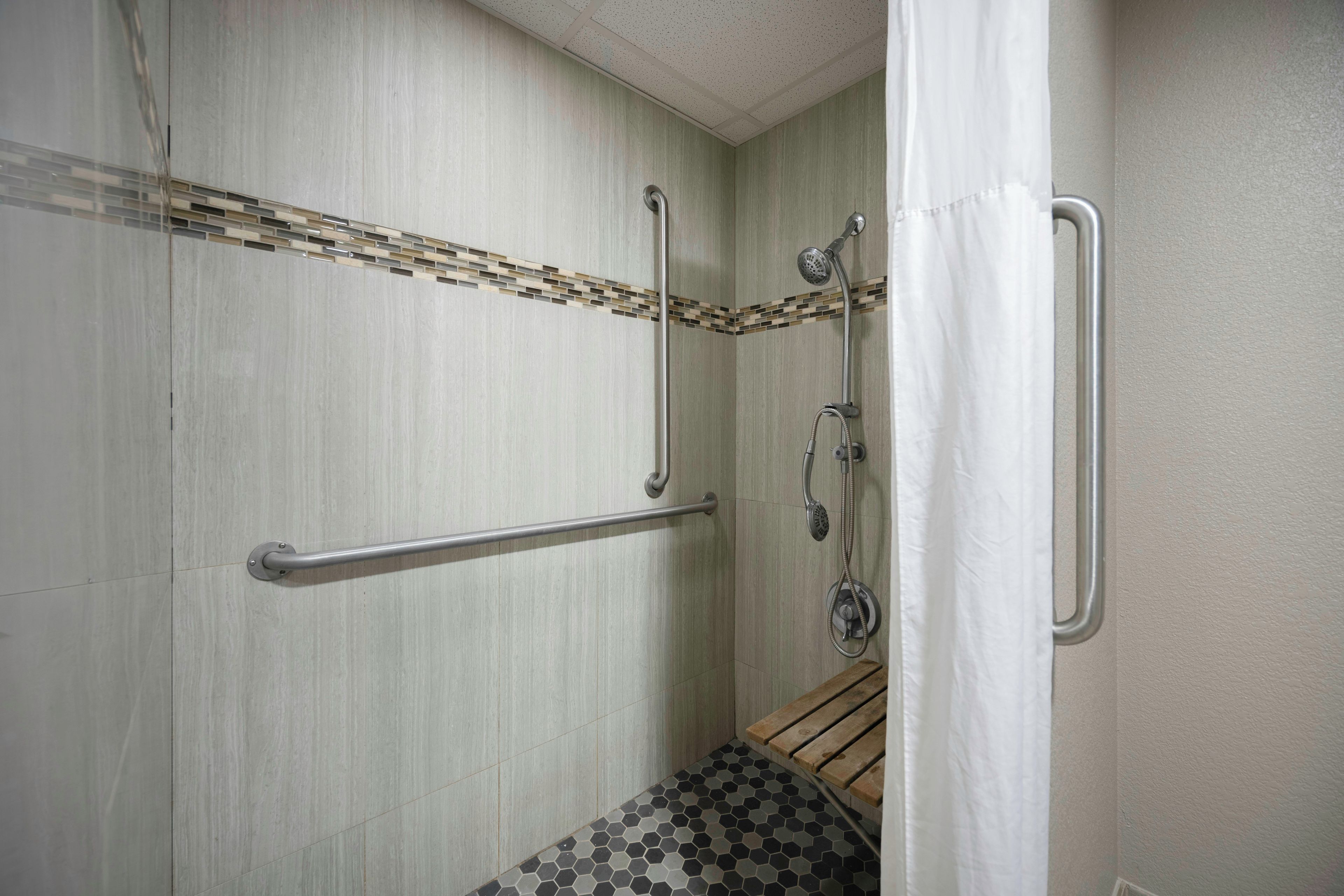 A shower with a grab bar, a showerhead, and a curtain.
