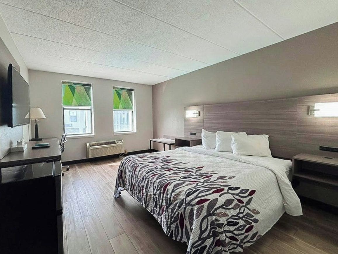 A hotel room with a bed, bedside tables, a desk, a lamp, and a flat-screen TV.