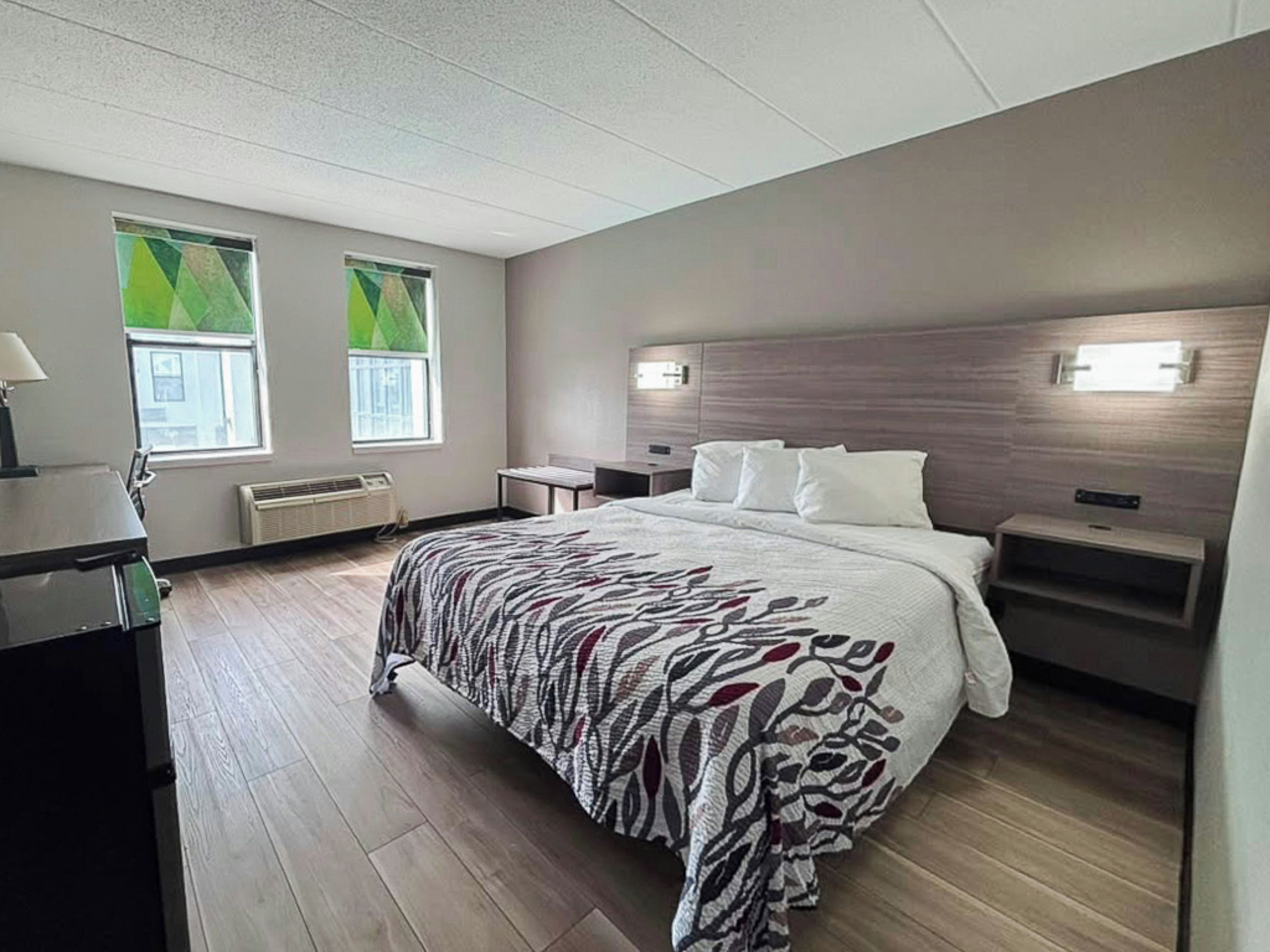 A modern hotel room with a large bed, bedside tables, a desk, and a window with blinds.