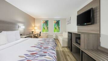Habitación de hotel con cama, escritorio, una silla, televisor y dos ventanas con arte abstracto.